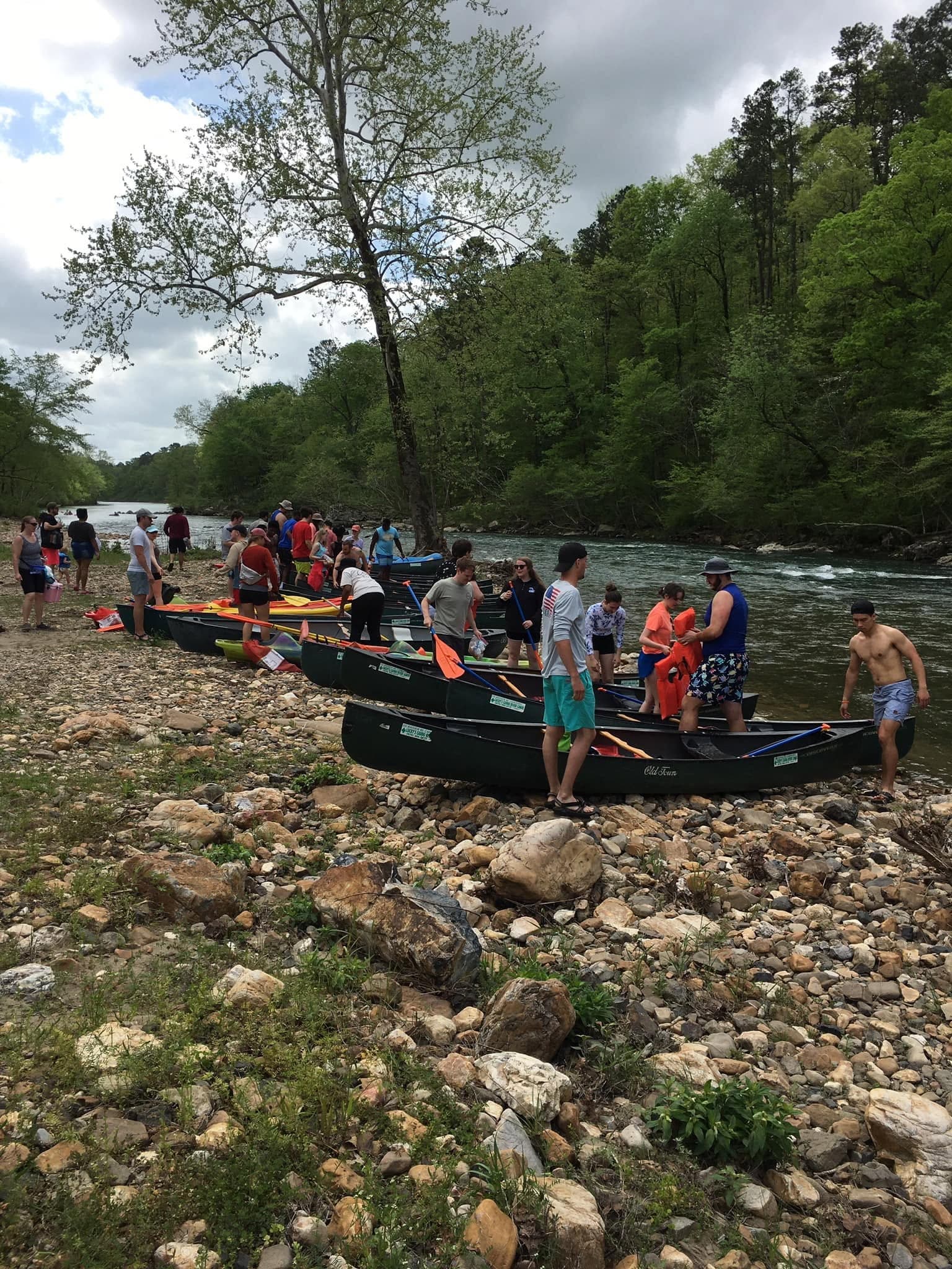 A large group preparing canoes along the rocky Caddo River shoreline